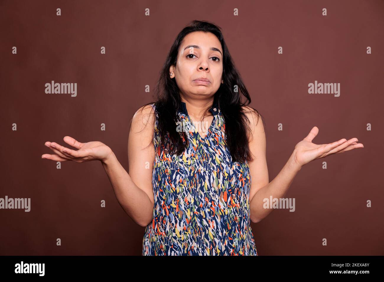 Puzzled indian woman shrugging shoulders with questioning facial expression portrait. Confused lady standing with hands spread wide, doubting, looking at camera, front view mid shot Stock Photo