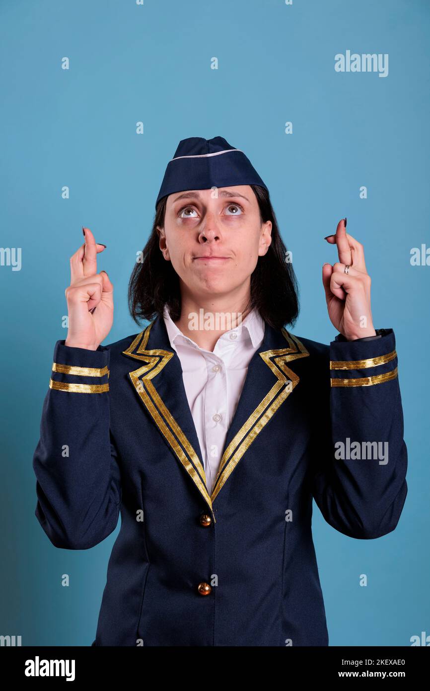 Portrait of prayer stewardess crossing fingers, looking up, praying for luck before flying. Superstitious flight attendant getting lucky, pleading for success with hopeful facial expression Stock Photo