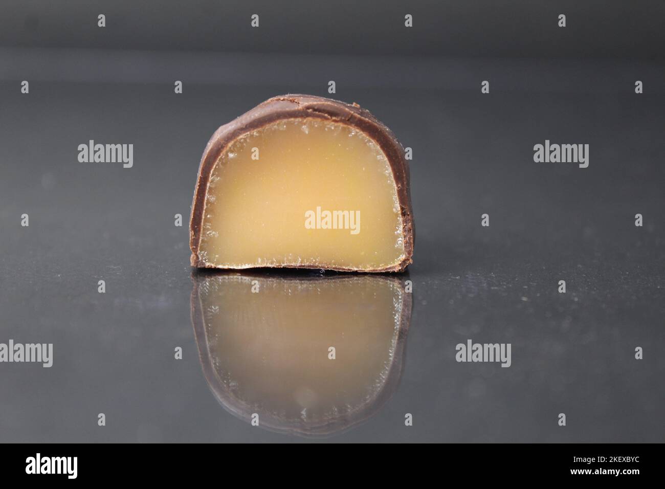 chocolate case candy in section with yellow brown fruit filling praline. Marmalade jelly candies in chocolate close-up on a black background. Chocolat Stock Photo