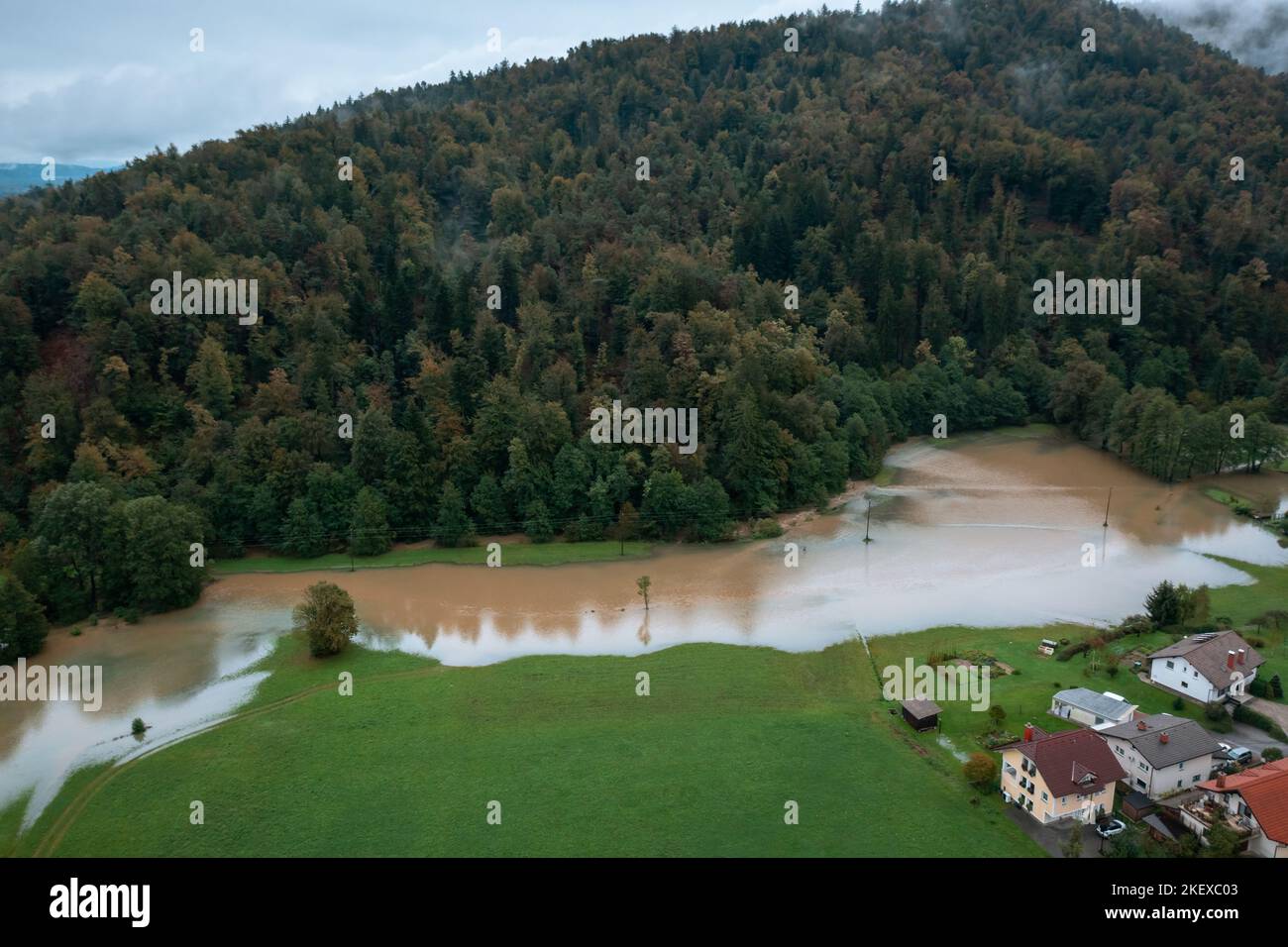 Heavy rainfall causing flooding, water moving slowly across river plains, farmland, and village