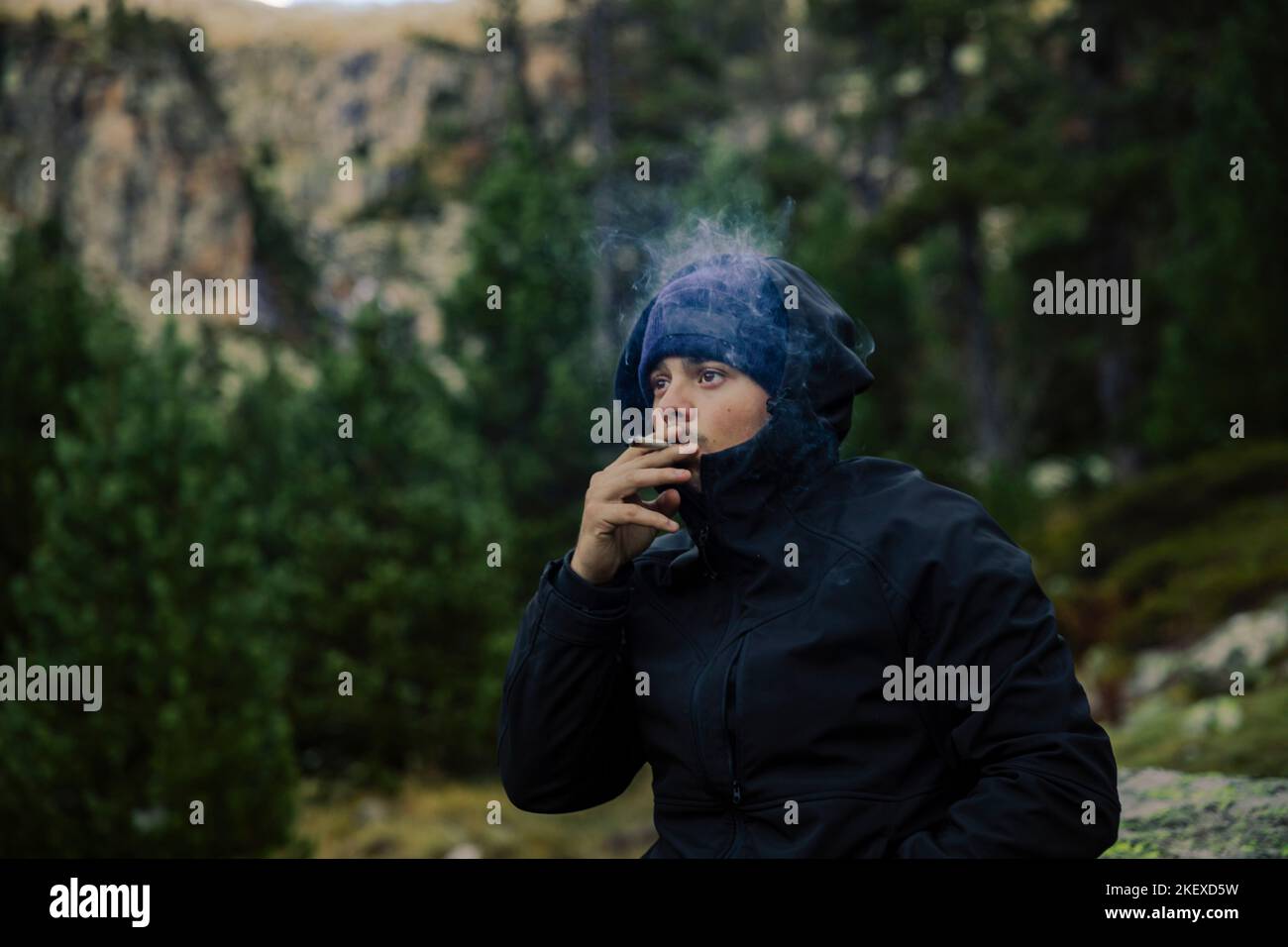 Boy with coat and hat smoking a marijuana cigarette in nature Stock Photo