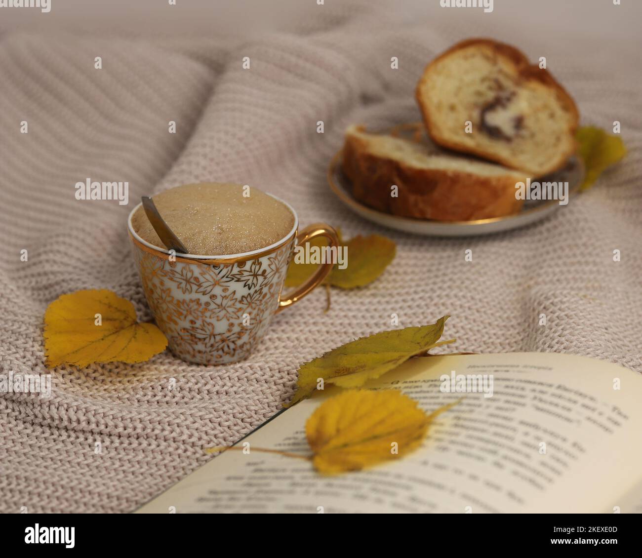 A cup of coffee on the table, an open book, a dessert, a warm sweater and yellow autumn leaves close-up, the concept of a cozy autumn morning Stock Photo