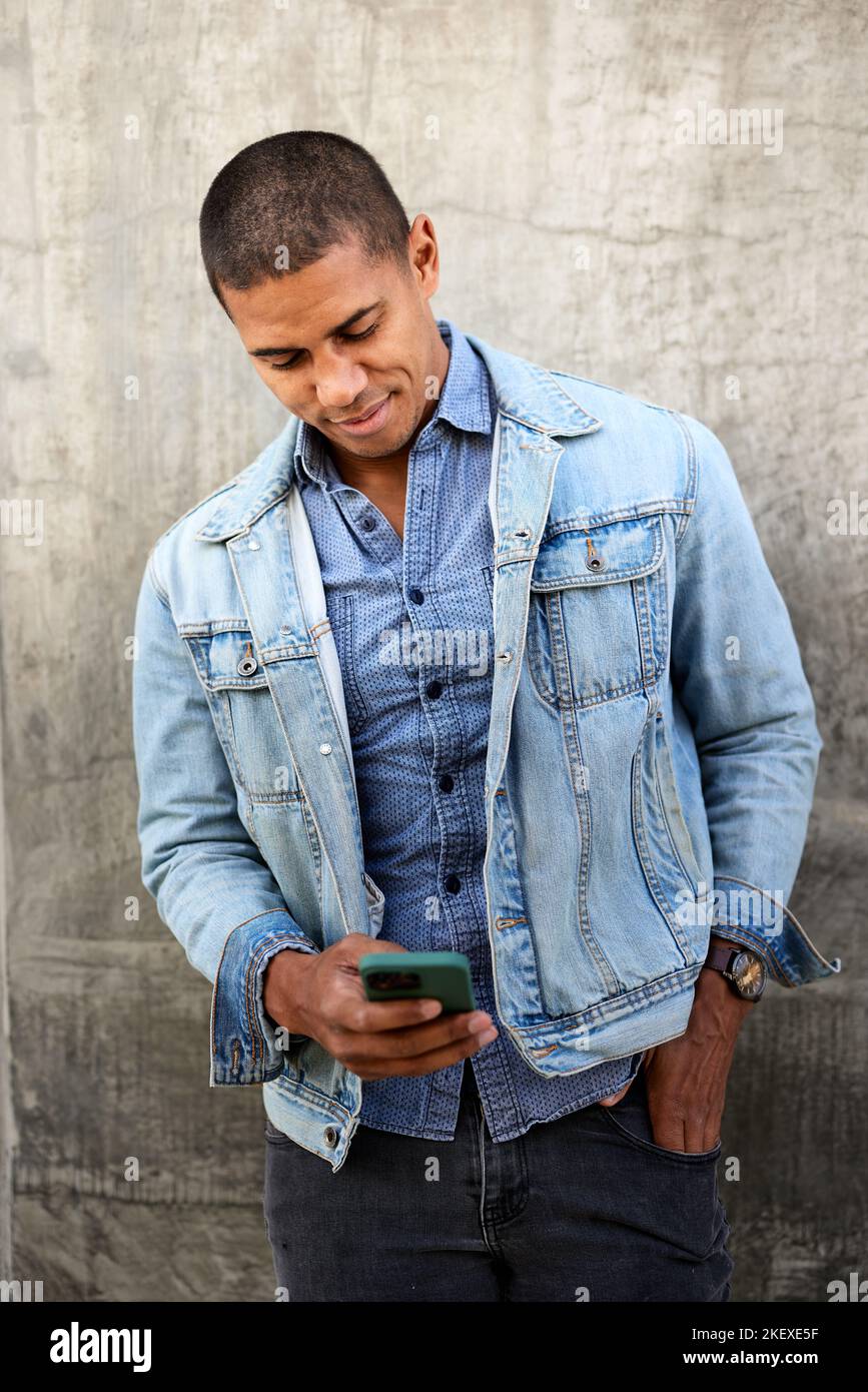 Man using smart phone standing against wall Stock Photo