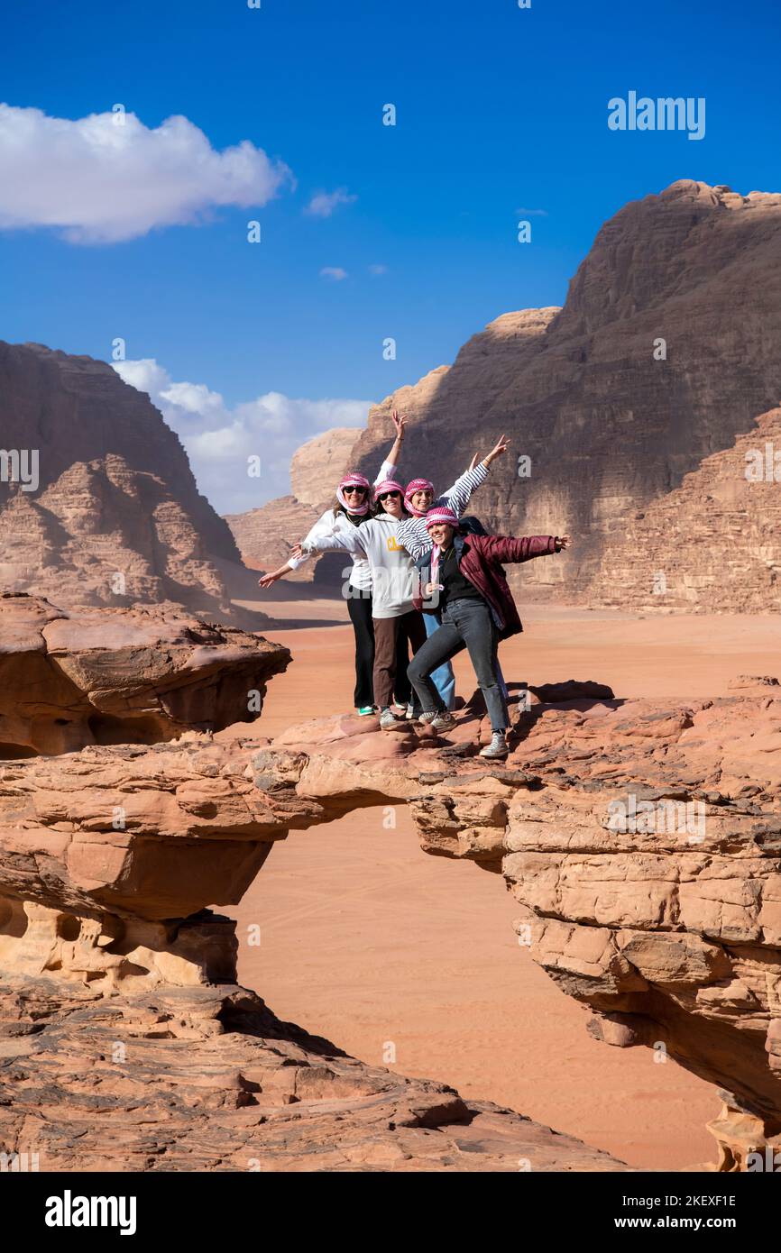 Four female tourists posing on rock bridge Wadi Rum Jordan Stock Photo