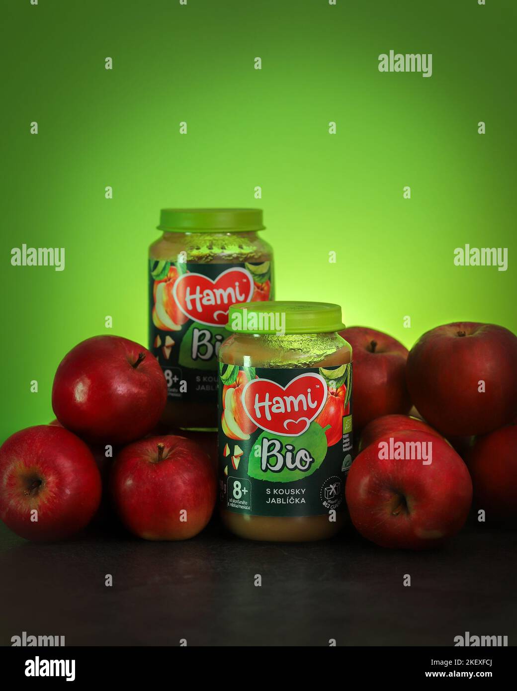 Children food. Applesauce in a glass jar Hami Bio and red ripe apples on a background. Selective focus, place for text. Stock Photo