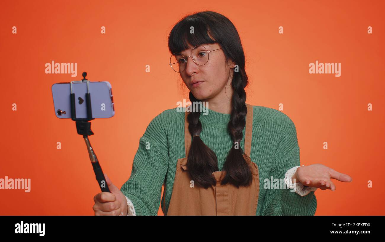 Kind Hectare Renovatie Young nerd woman with pigtails in glasses traveler blogger taking selfie on mobile  phone selfie stick, communicating video call online with subscribers. Latin  girl isolated on studio orange background Stock Photo -
