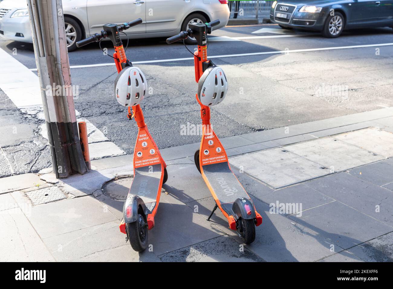 Neuron orange e electric scooters with helmets for hire on a pavement