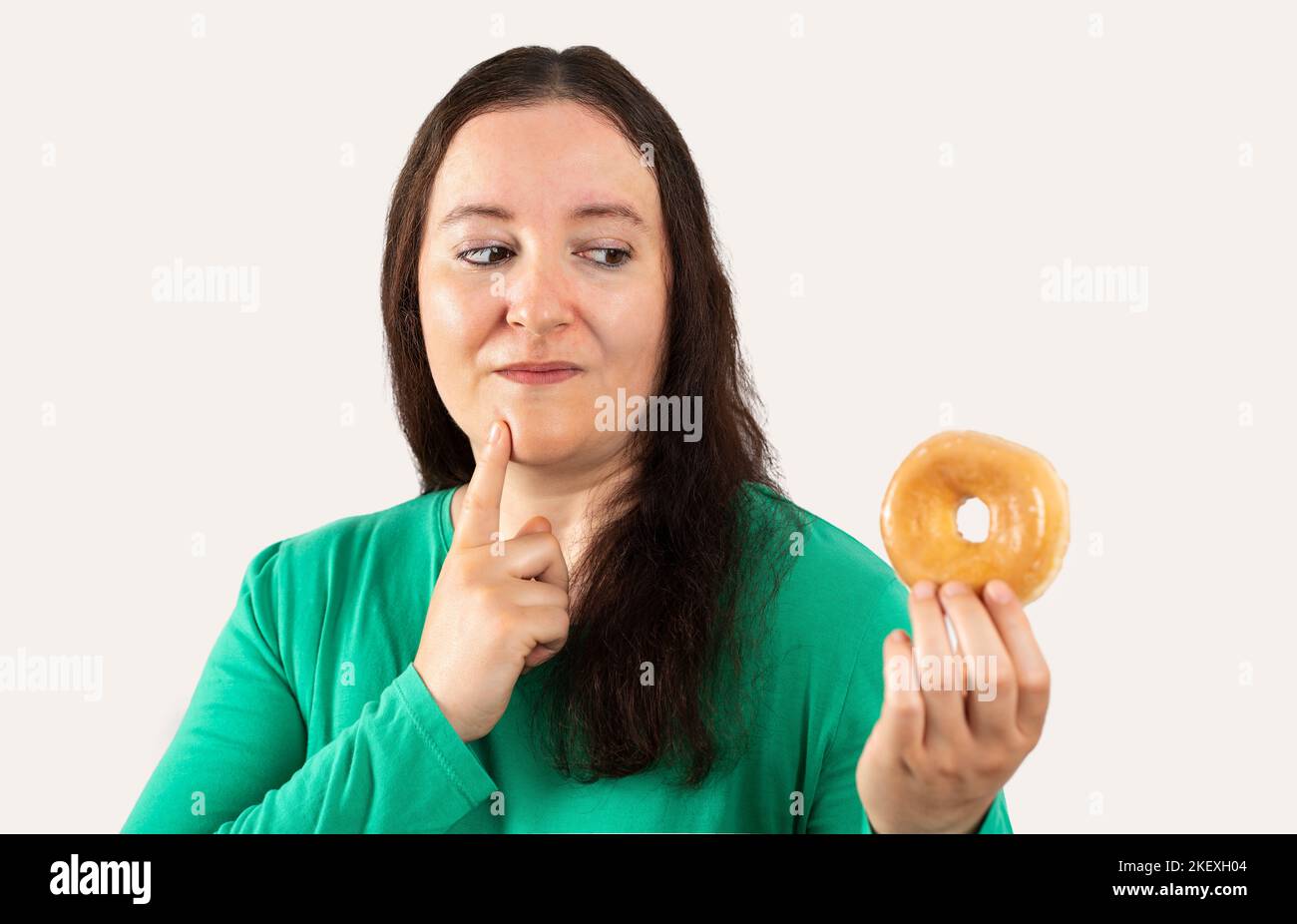 Middle age hispanic woman eating glazed donut over isolated white background serious face thinking about question, very confused idea Stock Photo