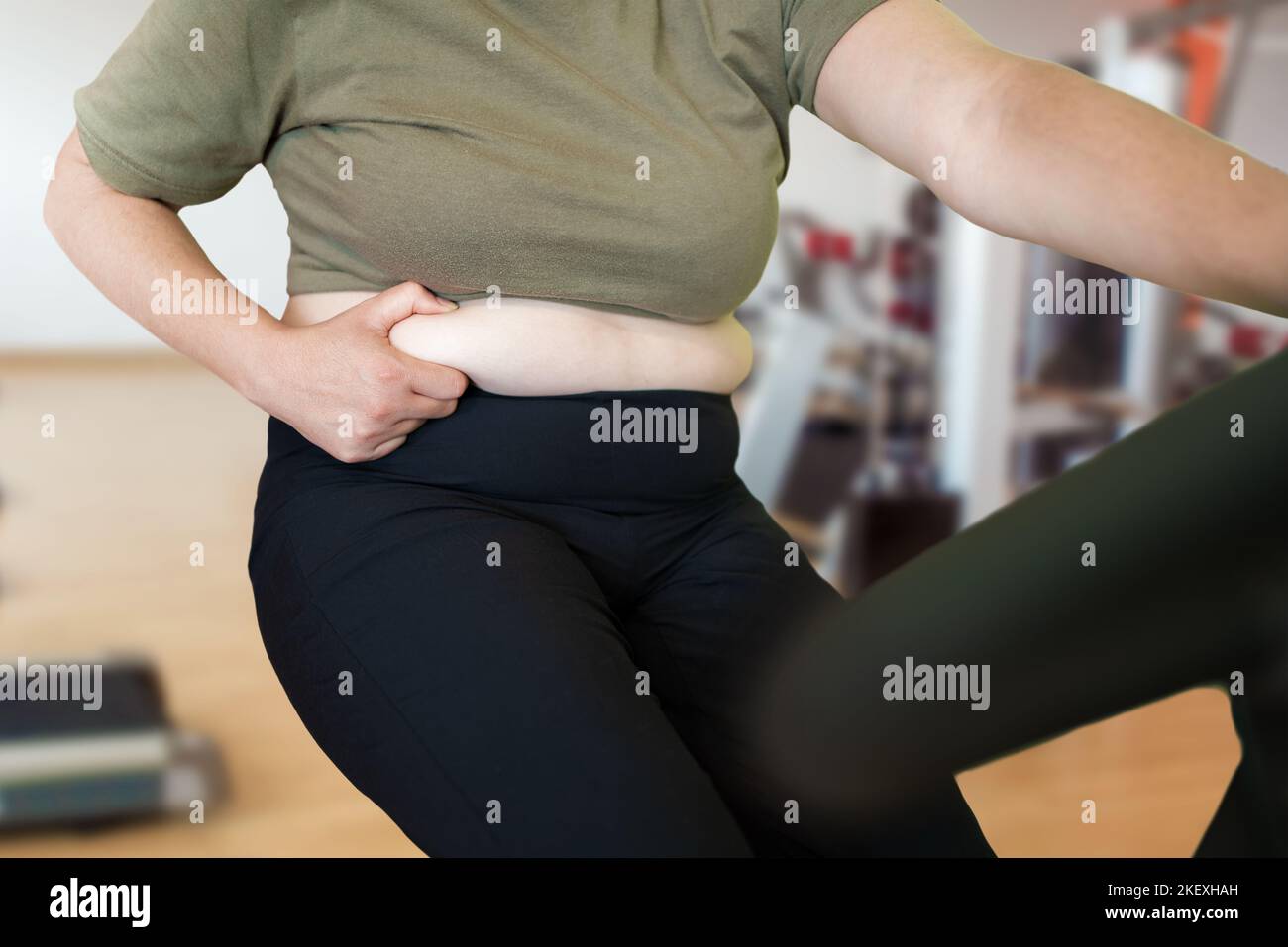 Shot of a young woman exercising at the gym on a stationary bike and pinching her fats Stock Photo