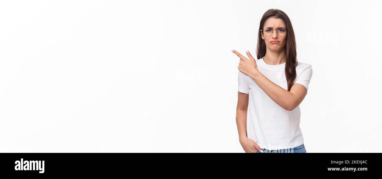 Waist-up portrait of moody, disappointed and complaining cute brunette woman in glasses, frowning and grimacing, sulking defensive, pointing finger Stock Photo
