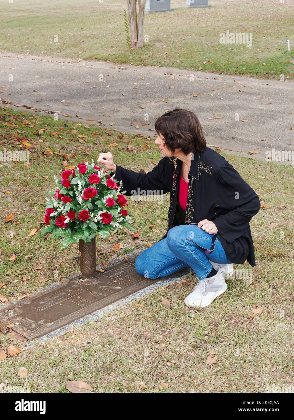 Mature woman placing flowers at a family grave site, as a memorial, in