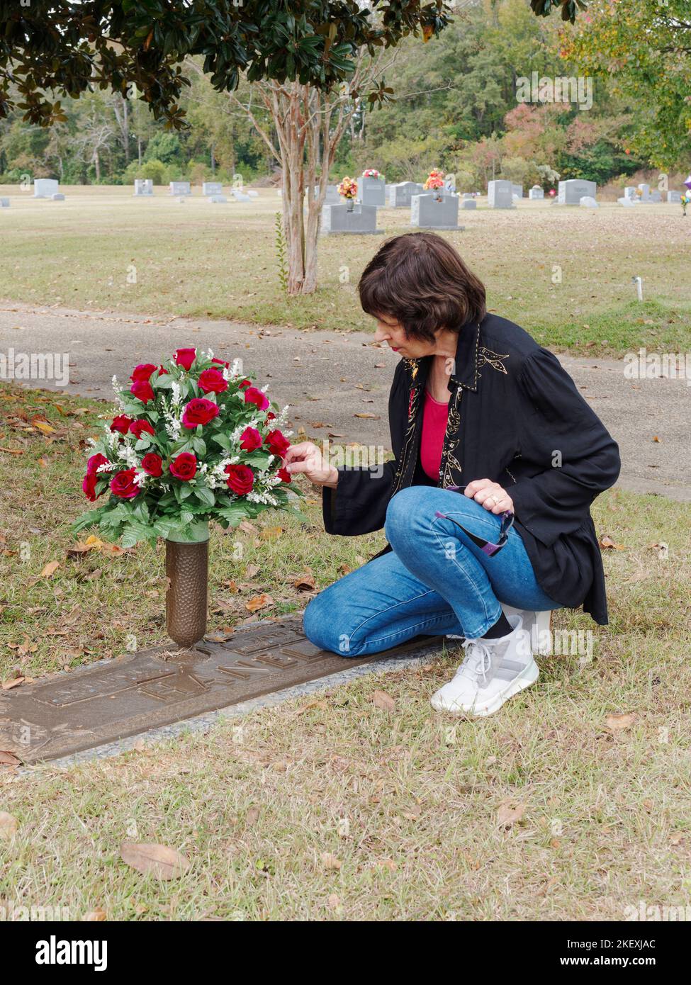 Mature woman placing flowers at a family grave site, as a memorial, in a cemetery in Montgomery Alabama, USA. Stock Photo