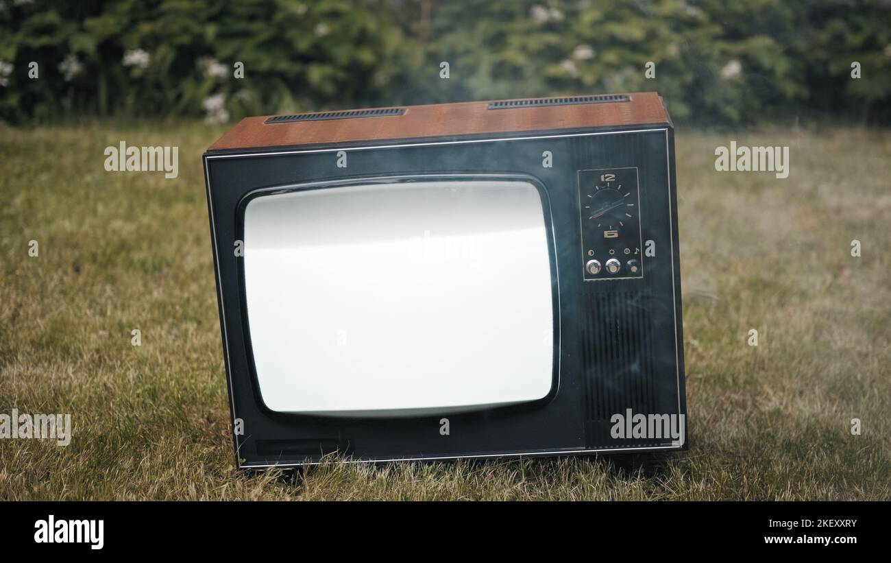 Old vintage retro TV stands on the grass. Smoke billows from the damaged device Stock Photo