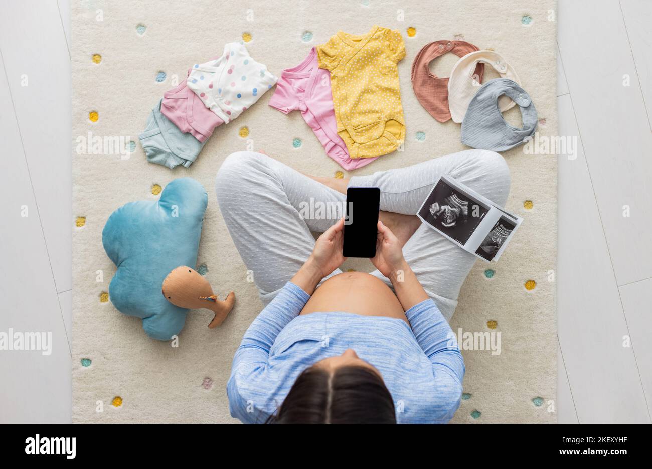 Pregnant woman using phone app for shopping, telemedicine reading about pregnancy or other. Black screen with copy space, baby clothing and toys Stock Photo