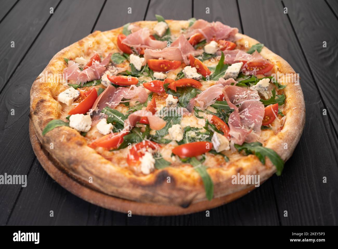 Traditional Italian prosciutto pizza with parmesan, bacon and arugula
