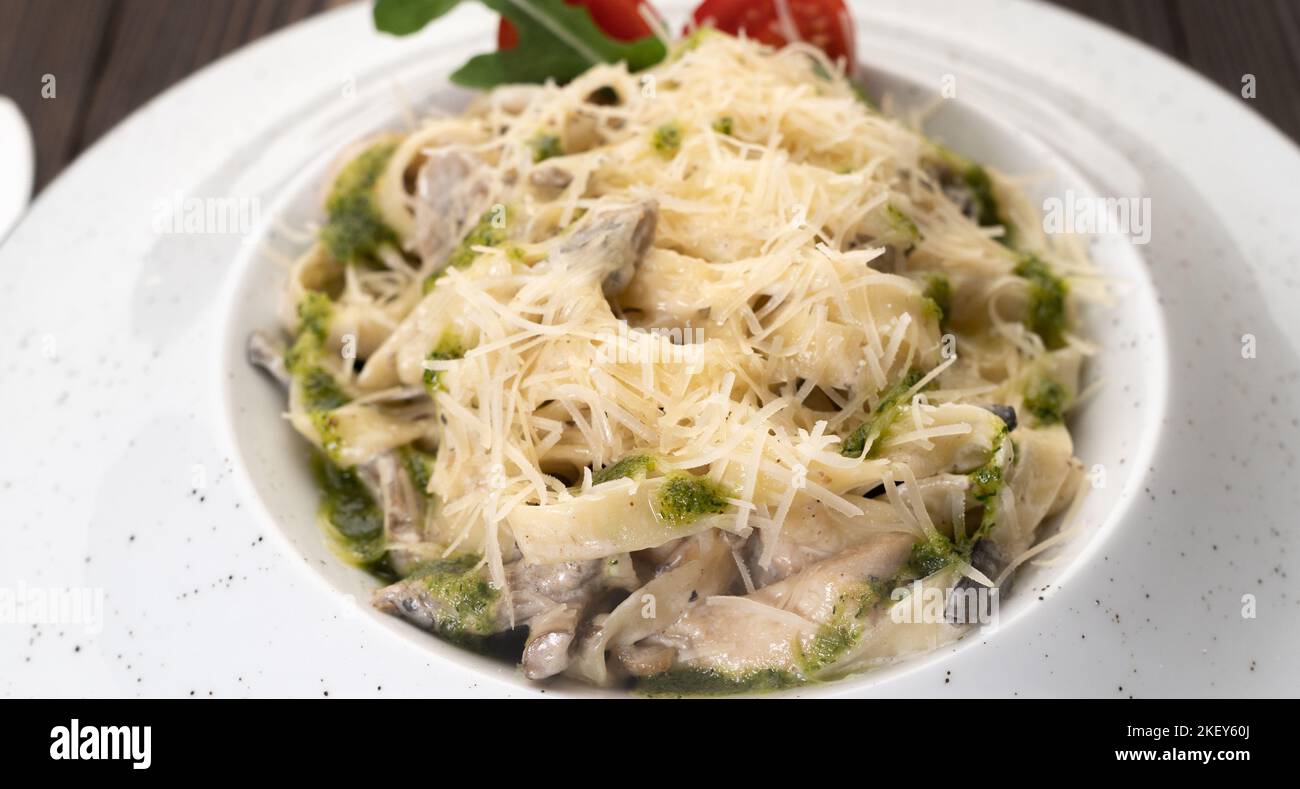 Plate of Italian creamy pasta with chicken and mushrooms decorated with basil sauce. Traditional Italian lunch Stock Photo