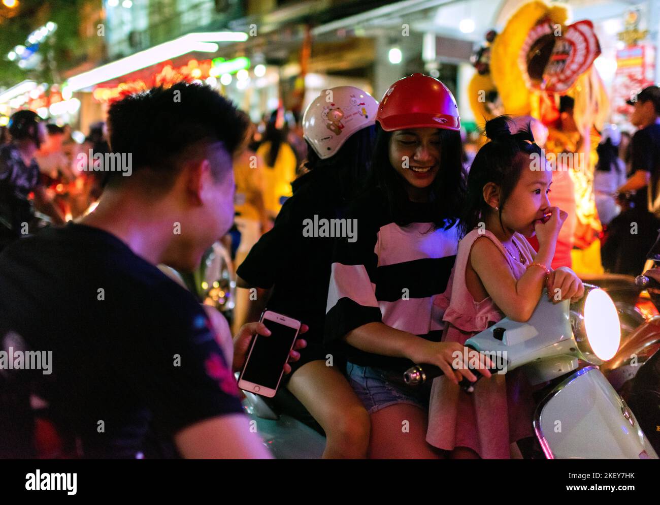 Cat Ba Island, Halong Bay, Vietnam; September 22, 2018: Young girl smiles at young man as she rides a scooter through heavy traffic on a holiday stree Stock Photo