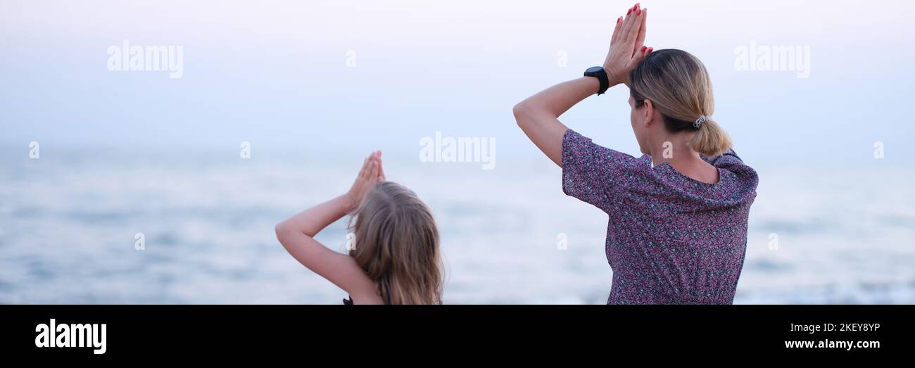 Mom and daughter doing yoga and sitting in lotus position on seashore ...