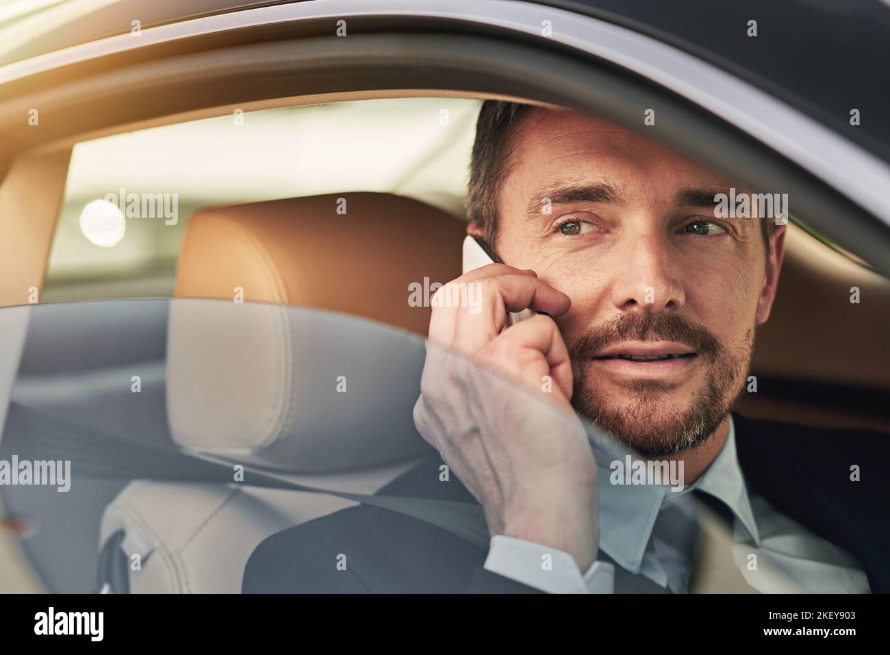 Ill be there shortly. a handsome businessman talking on his cellphone while driving into work. Stock Photo