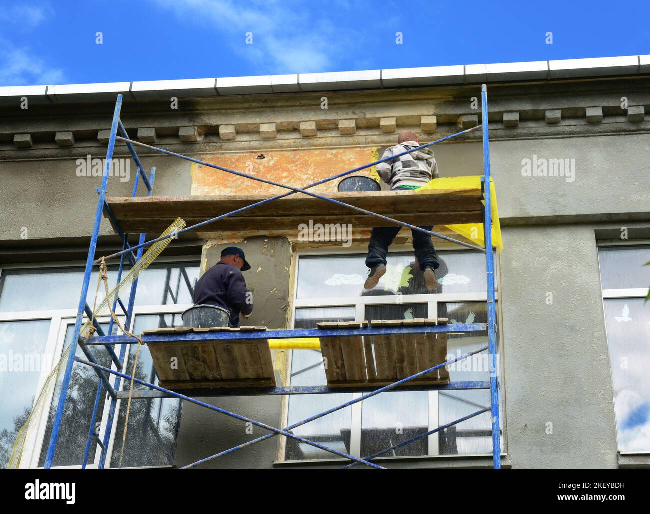 The building contractors are plastering and painting a stucco facade of