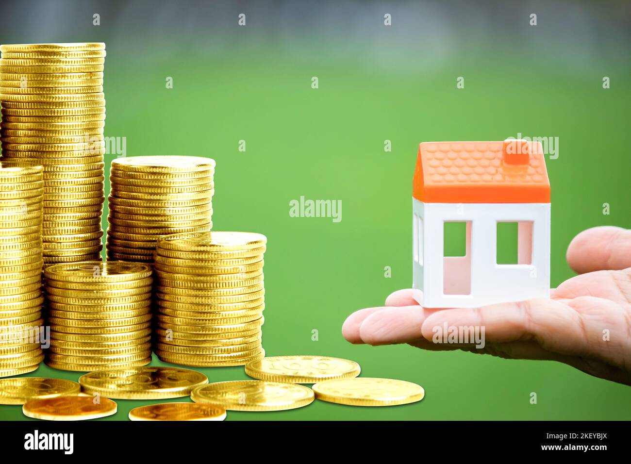 Idea concept of saving money to buy house. Stacked coins and figure of house in one's hand isolated on green background. Real estate value increase. Stock Photo