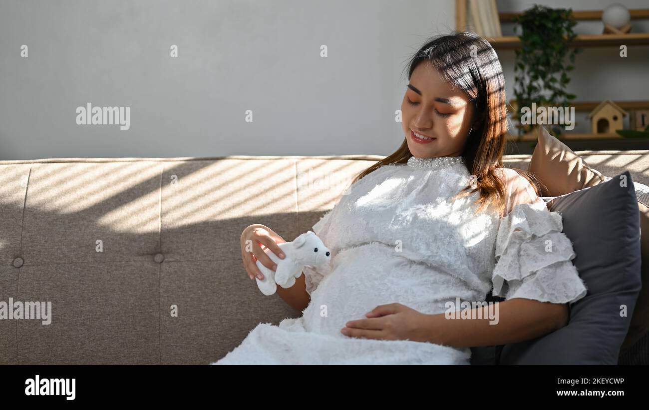 Happy young Asian pregnant woman relaxing on sofa in the living room