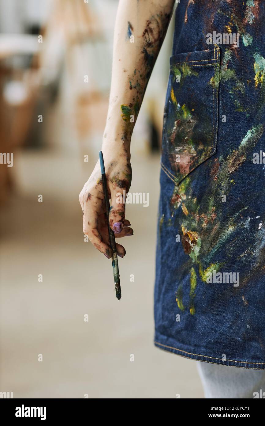 Hand of young creative female painter in denim apron holding paintbrush ...