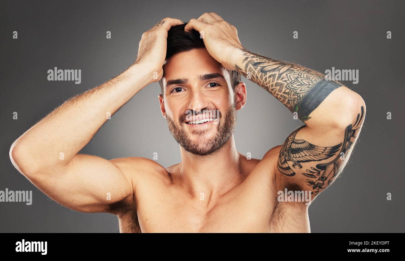 Face, tattoo and beauty with a man model in studio on a gray background for wellness with confidence. Portrait, happy and smile with a handsome young Stock Photo
