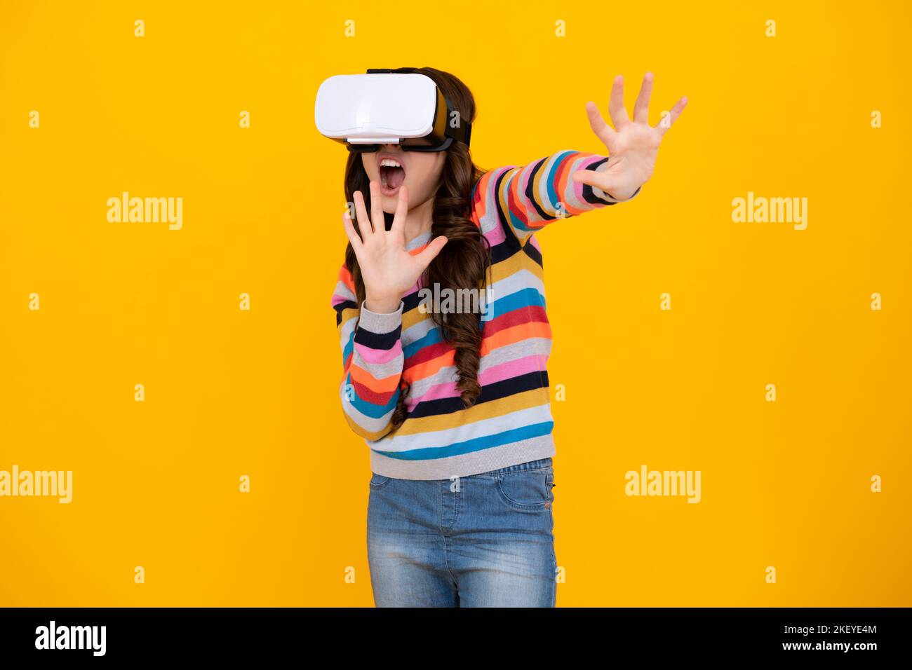Portrait of young teen girl in VR helmet, isolated on yellow. Gamer