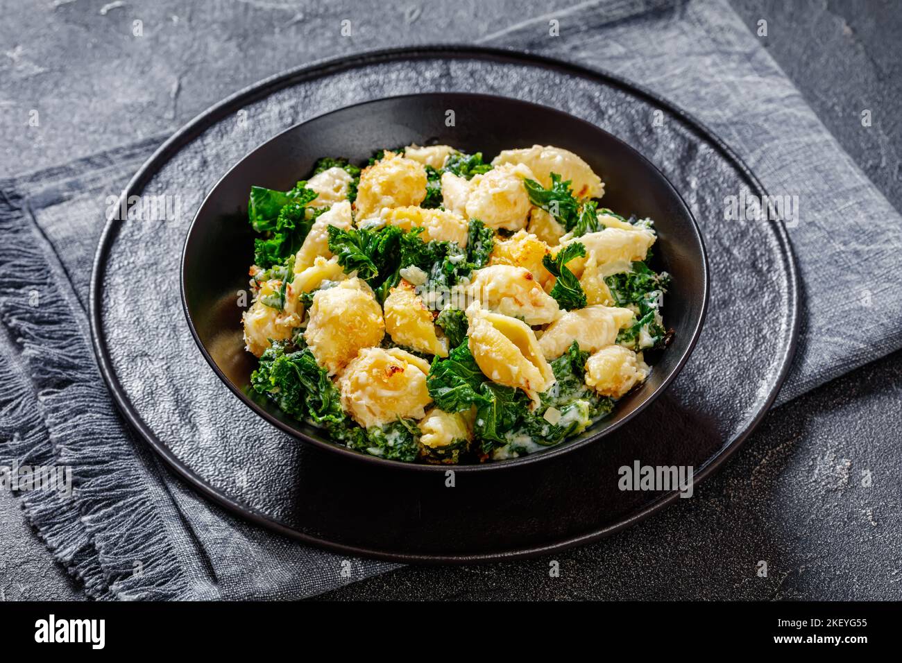 portion of cheesy baked shell pasta with green leafy kale topped with ...