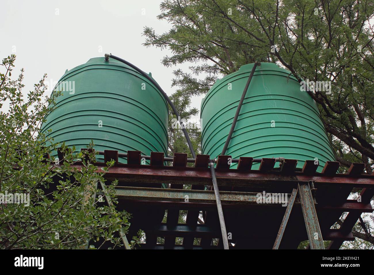 https://c8.alamy.com/comp/2KEYH21/two-big-green-plastic-water-storage-tanks-on-metal-stand-image-taken-from-below-feeder-pipes-visible-2KEYH21.jpg