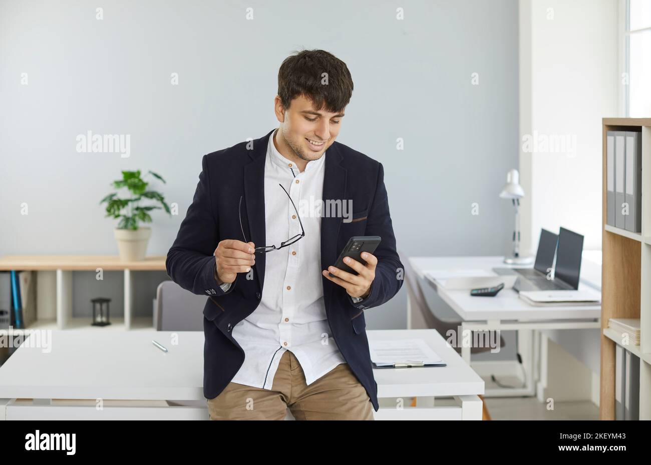 Young businessman standing in office and using online banking app on mobile phone Stock Photo