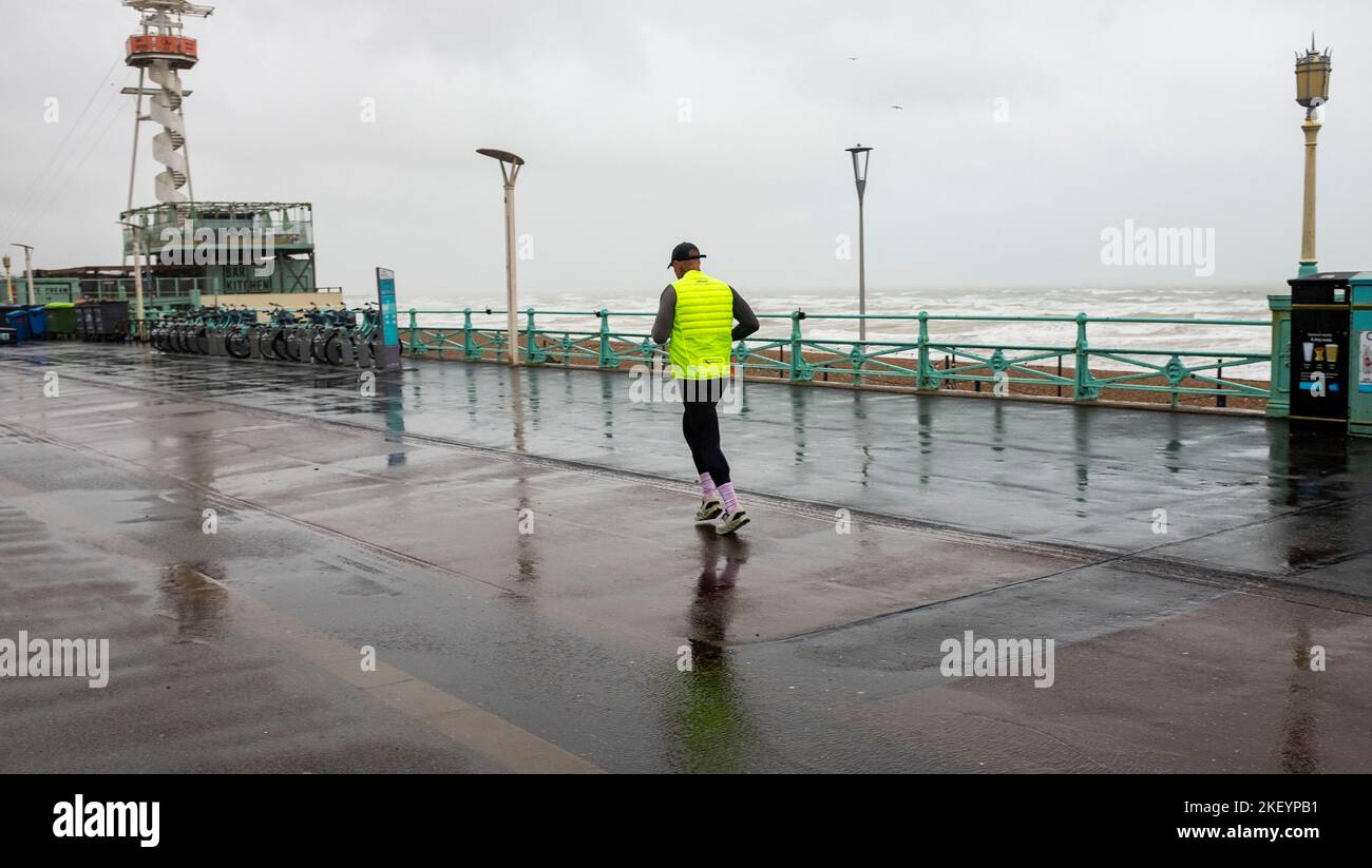 Brighton UK 15th November 2022 - A runner battles against the wind and rain on Brighton seafront as storms sweep across the South Coast this morning : Credit Simon Dack / Alamy Live News Stock Photo