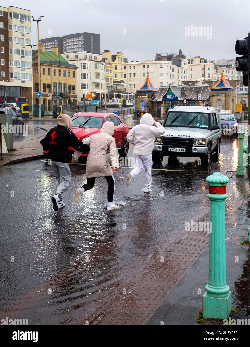 Brighton UK 15th November 2022 - Pedestrians try to dodge the rain and puddles on Brighton seafront during heavy rain and strong winds as storms sweep across the South Coast this morning : Credit Simon Dack / Alamy Live News Stock Photo