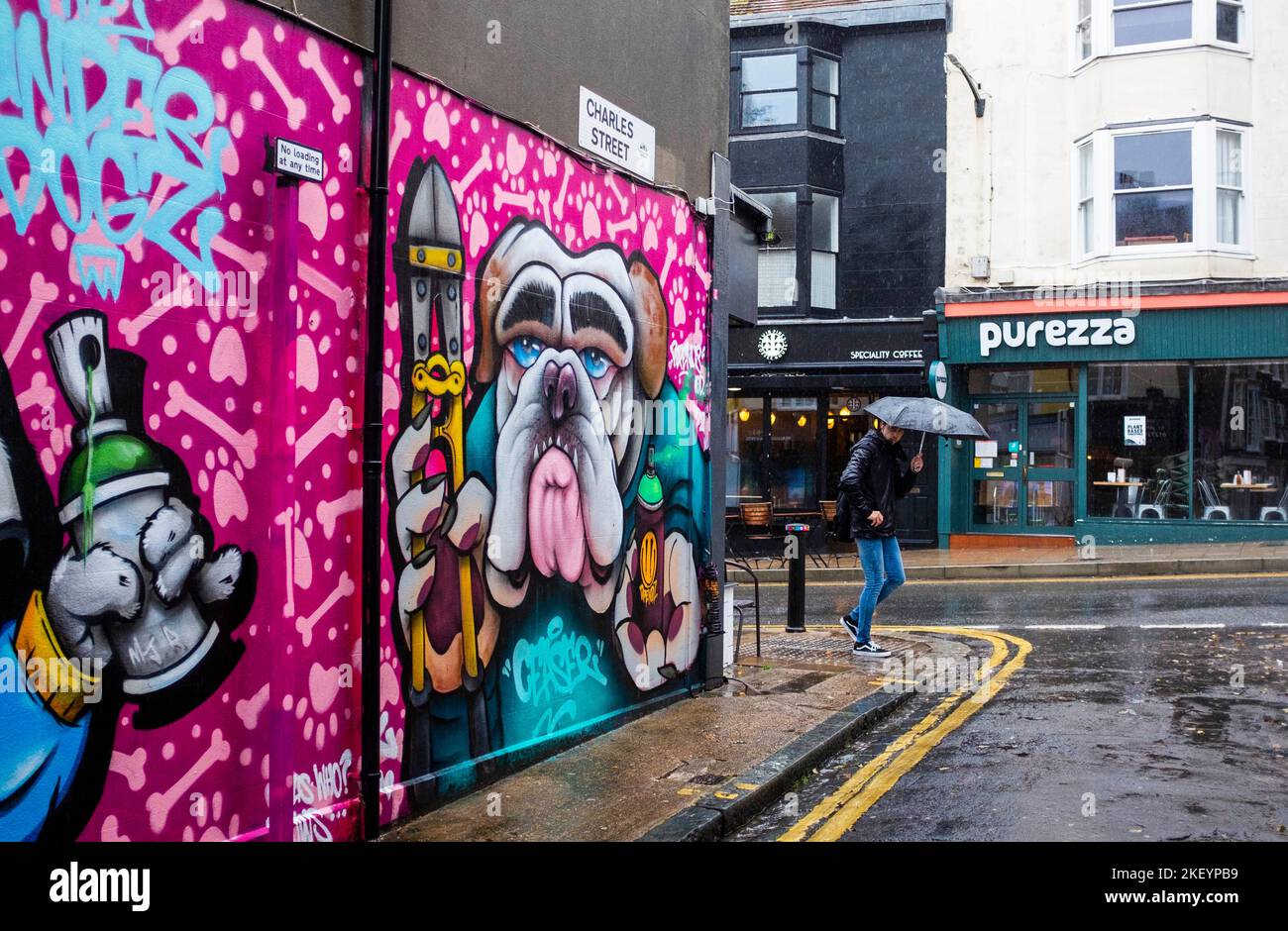 Brighton UK 15th November 2022 - A pedestrian with an umbrella passes by a colourful mural in Brighton as storms sweep across the South Coast this morning : Credit Simon Dack / Alamy Live News Stock Photo