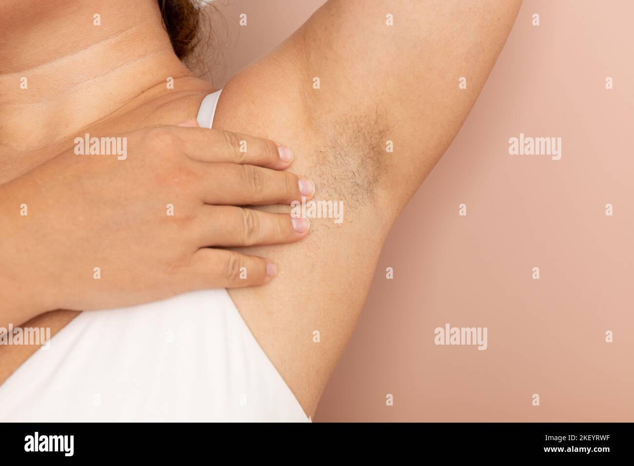 Woman touch hairy underarms with hand closeup, free copy space, beige background. Raised arm with armpit hair. Female beauty trend, freedom, feminism Stock Photo