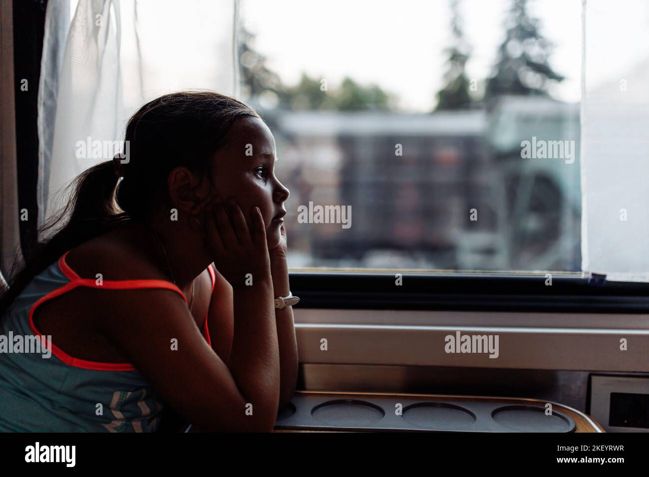 Pensive, wistful little tourist girl in cozy and comfortable train look out the window. Travelling and active lifestyle Stock Photo