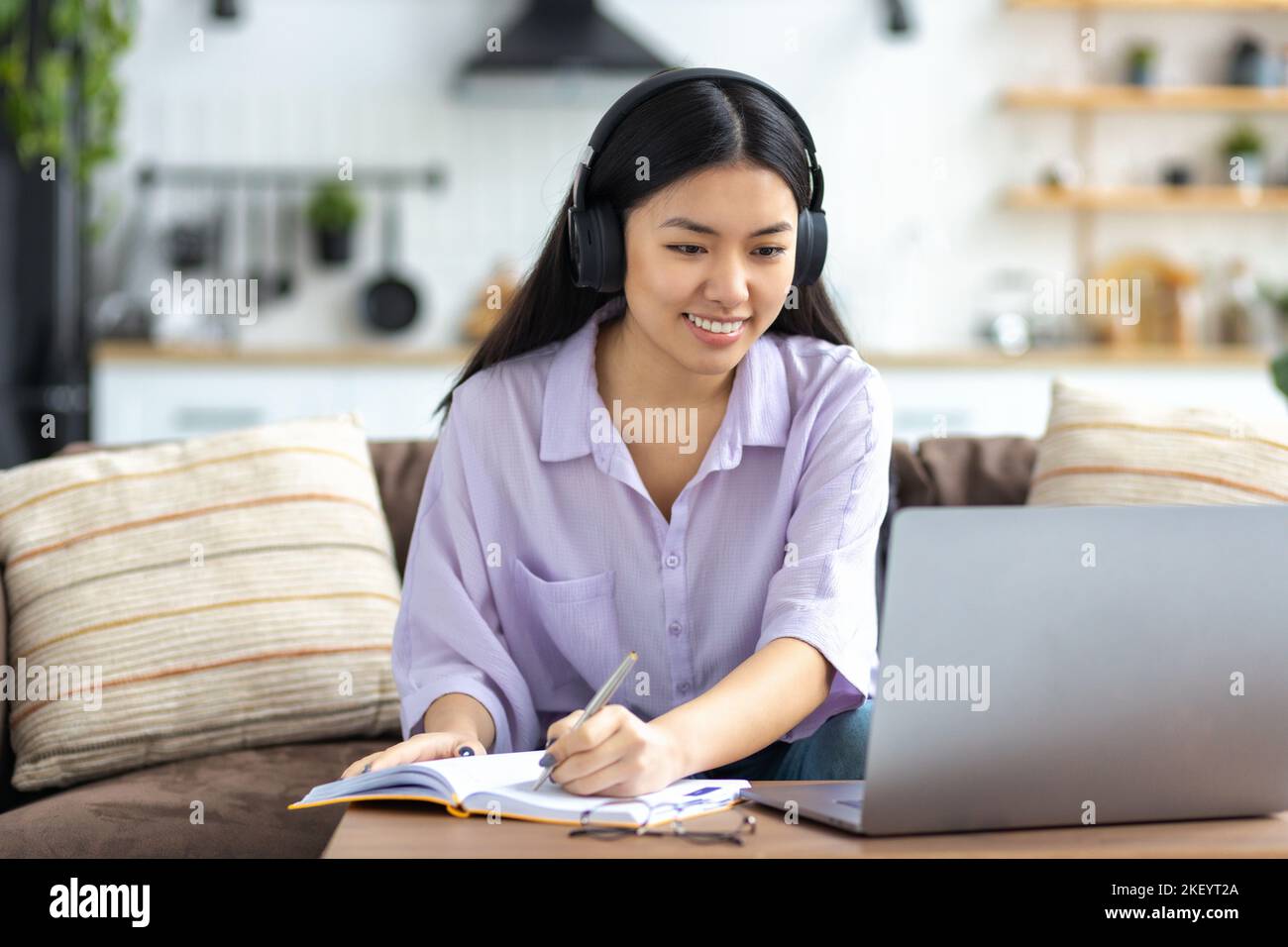 female student studying remotely using a laptop, taking notes on notepad during online lesson, e-learning Stock Photo