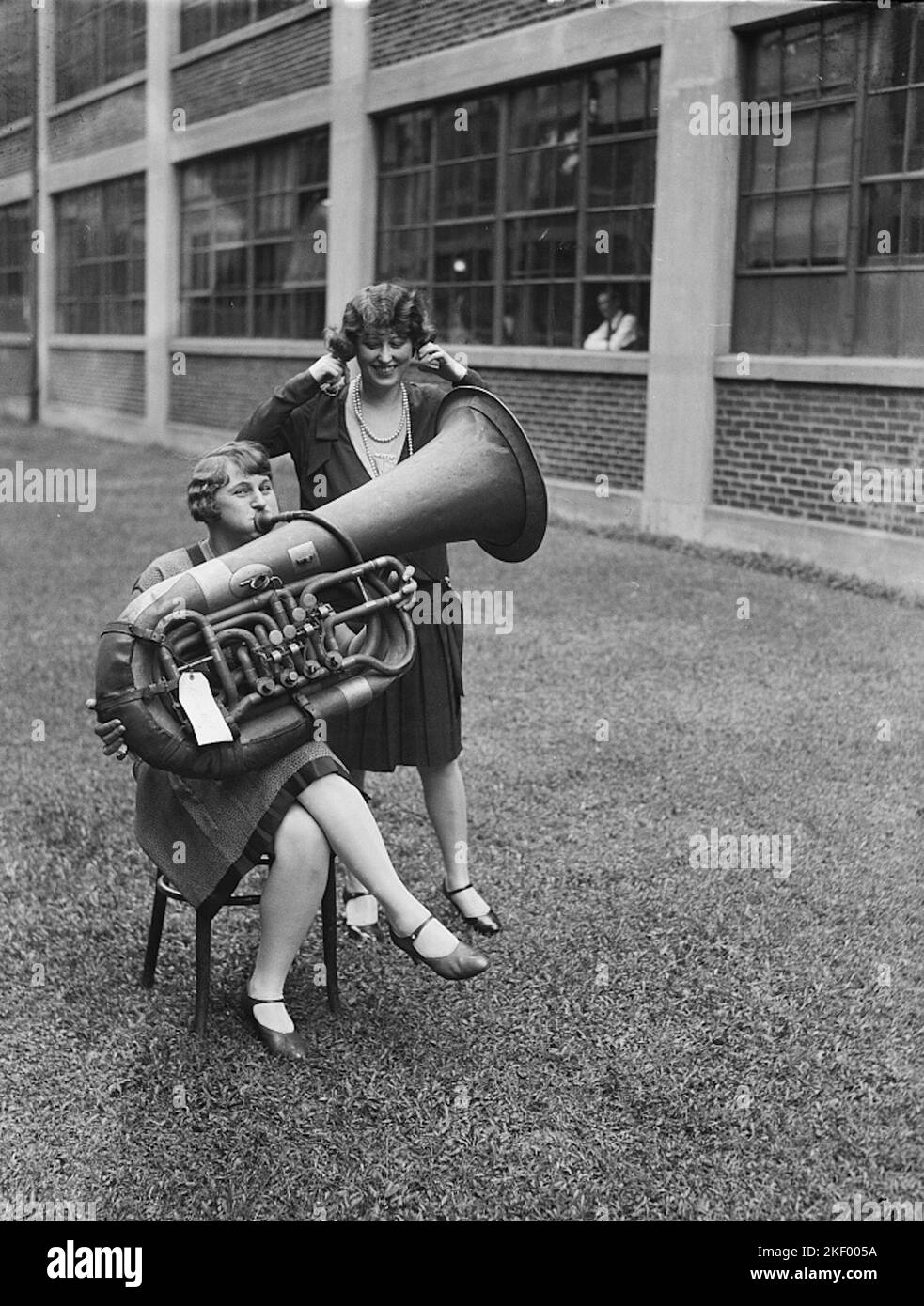 Tube Player - Humorous Photograph of a Woman Playing a Tuba with Another Woman with her Fingers in her Ears - 1928 Stock Photo