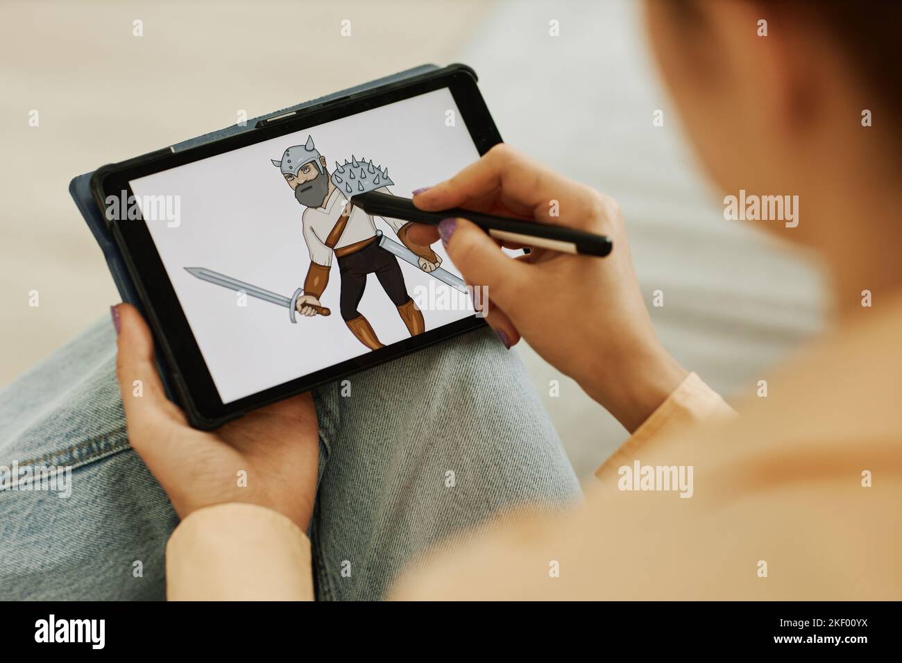 Selective focus on graphic picture of warrior on screen of tablet held by young female digital artist with stylus creating new images Stock Photo