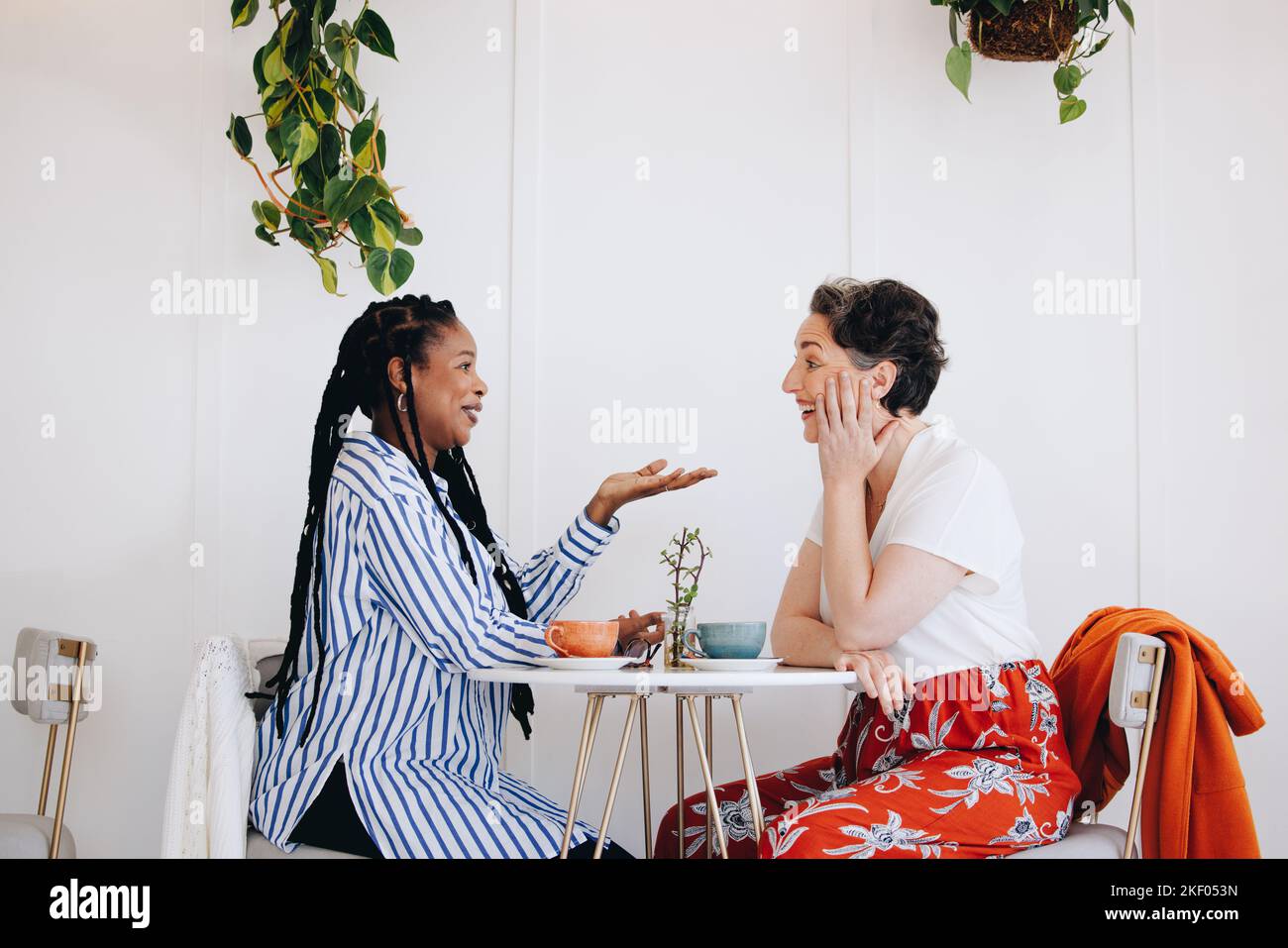 Happy female colleagues having a friendly conversation over coffee in a cafe. Two cheerful businesswomen having a chatty coffee break in a modern work Stock Photo