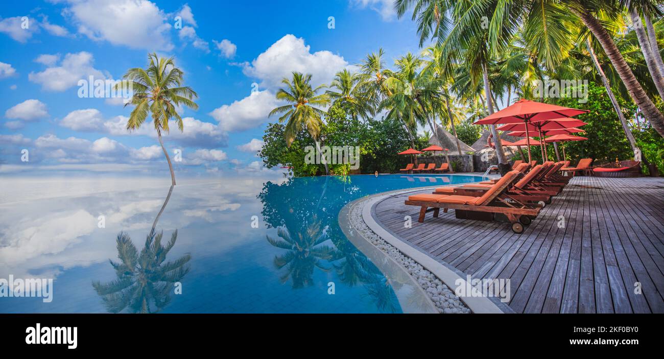 Luxurious beach resort with swimming pool seaside beach chairs or loungers under umbrellas with palm trees and blue sky. Summer travel hotel vacation Stock Photo
