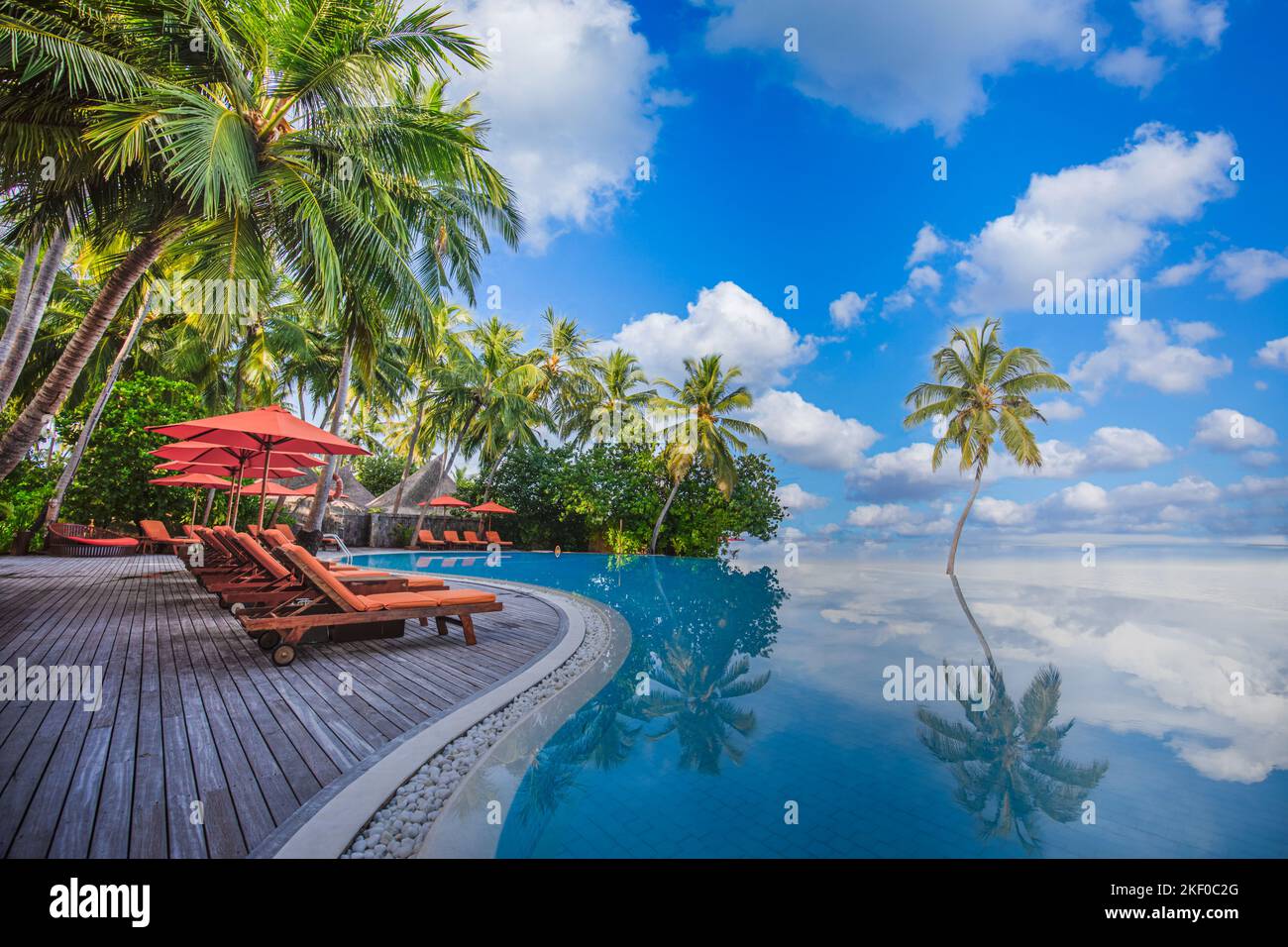 Luxurious beach resort with swimming pool seaside beach chairs or loungers under umbrellas with palm trees and blue sky. Summer travel hotel vacation Stock Photo
