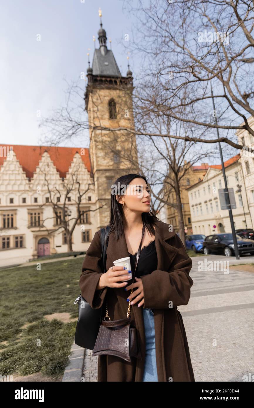 Tourist with paper cup walking on urban street and looking away in ...
