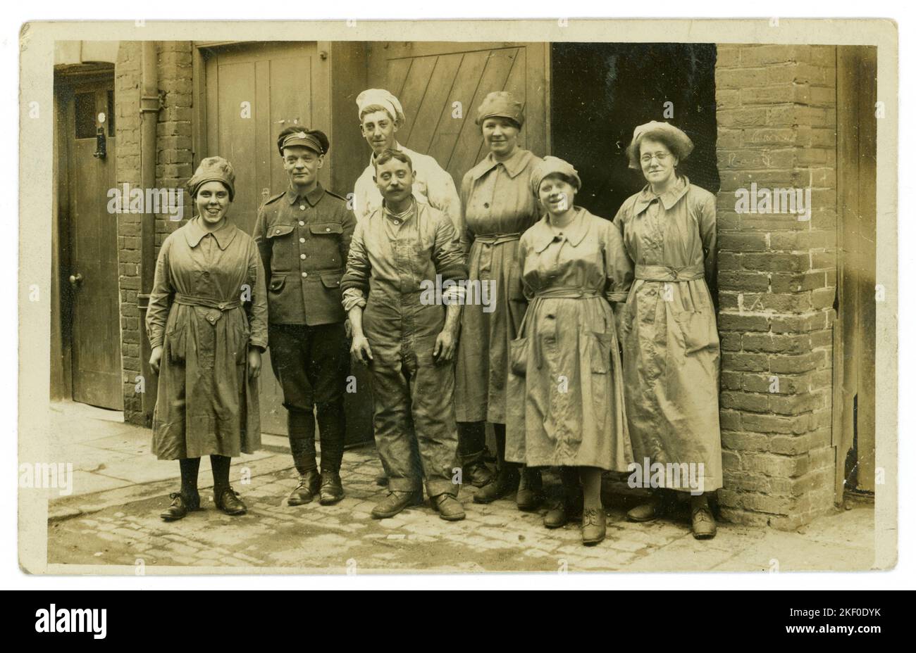 Original WW1 era postcard of group of army caterers both male and female from expeditionary force canteen or maybe the bakery all seem to be happy and enjoying themselves, one of he girls is cheeky and poking out her tongue. Lots of characters. The man in uniform is wearing an Army Service Corps (A.S.C.) badge on his postcard back design indicates the U.K., maybe at a training camp. Stock Photo