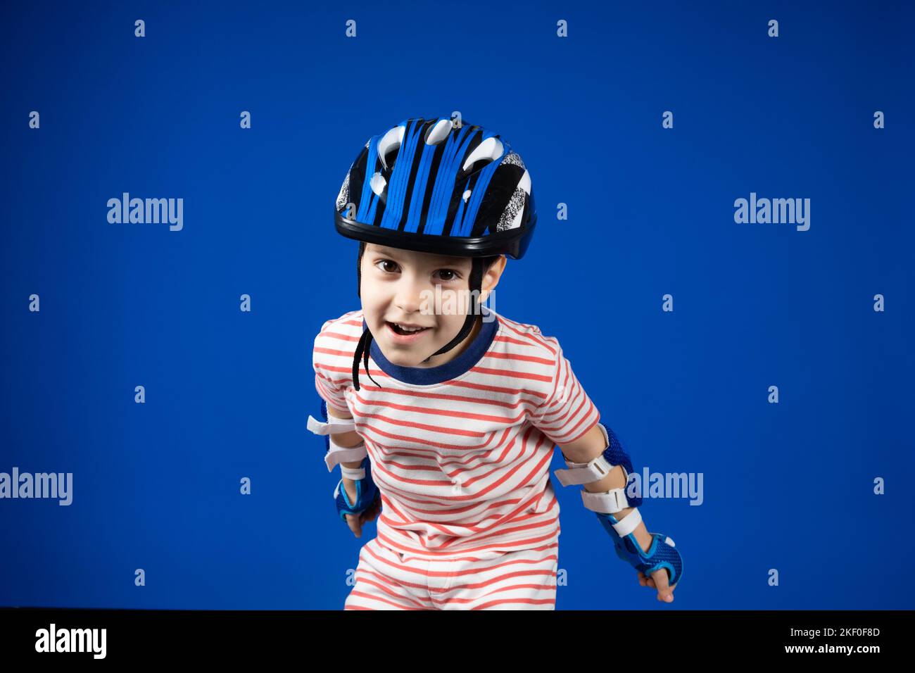 A happy boy in a protective helmet, elbow pads and gloves on a blue background. Protection when riding a bicycle, skateboard, roller skate Stock Photo