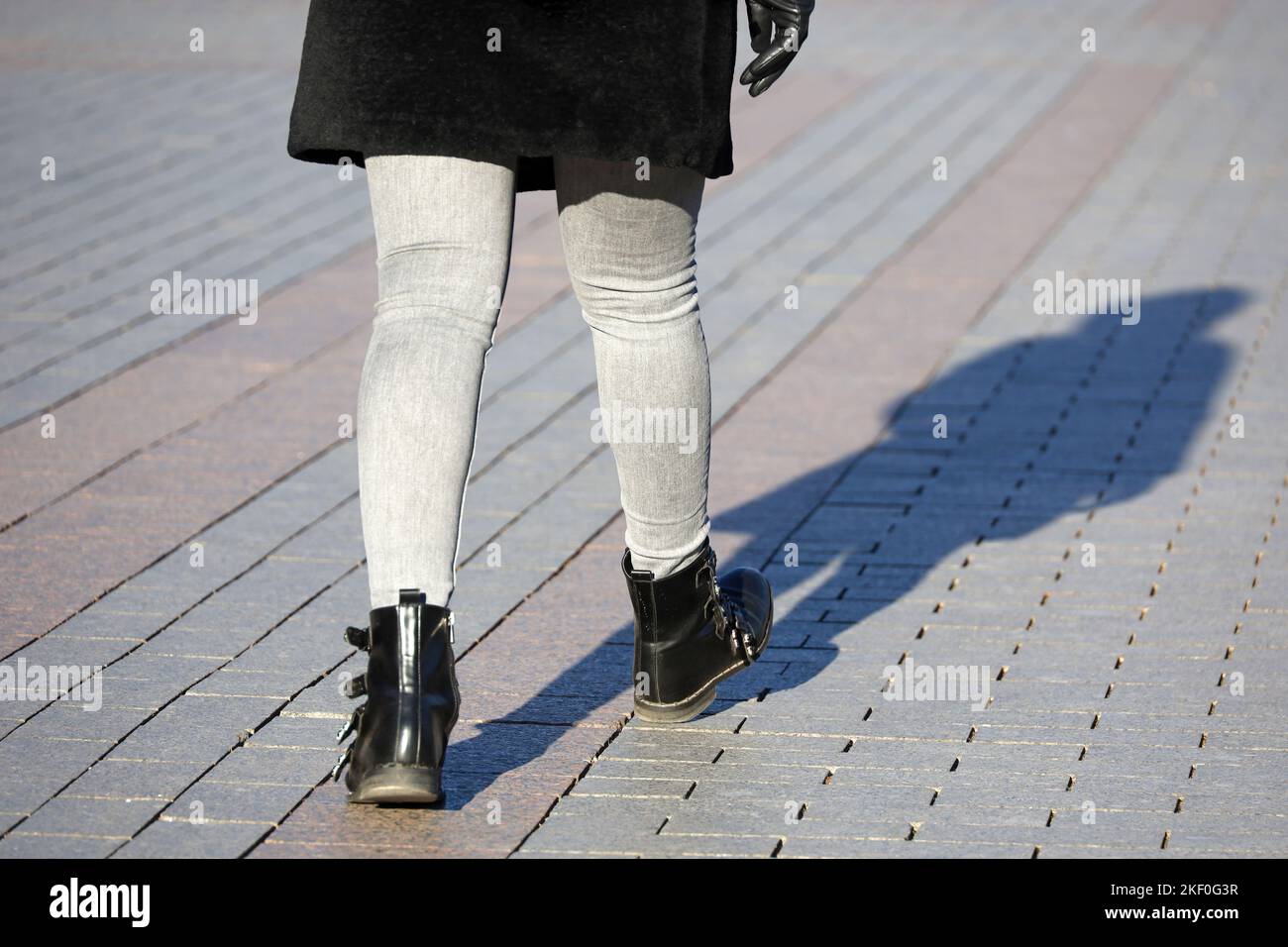 Female legs in black boots and jeans. Woman in warm coat walking on a street, fashion in autumn or winter city Stock Photo