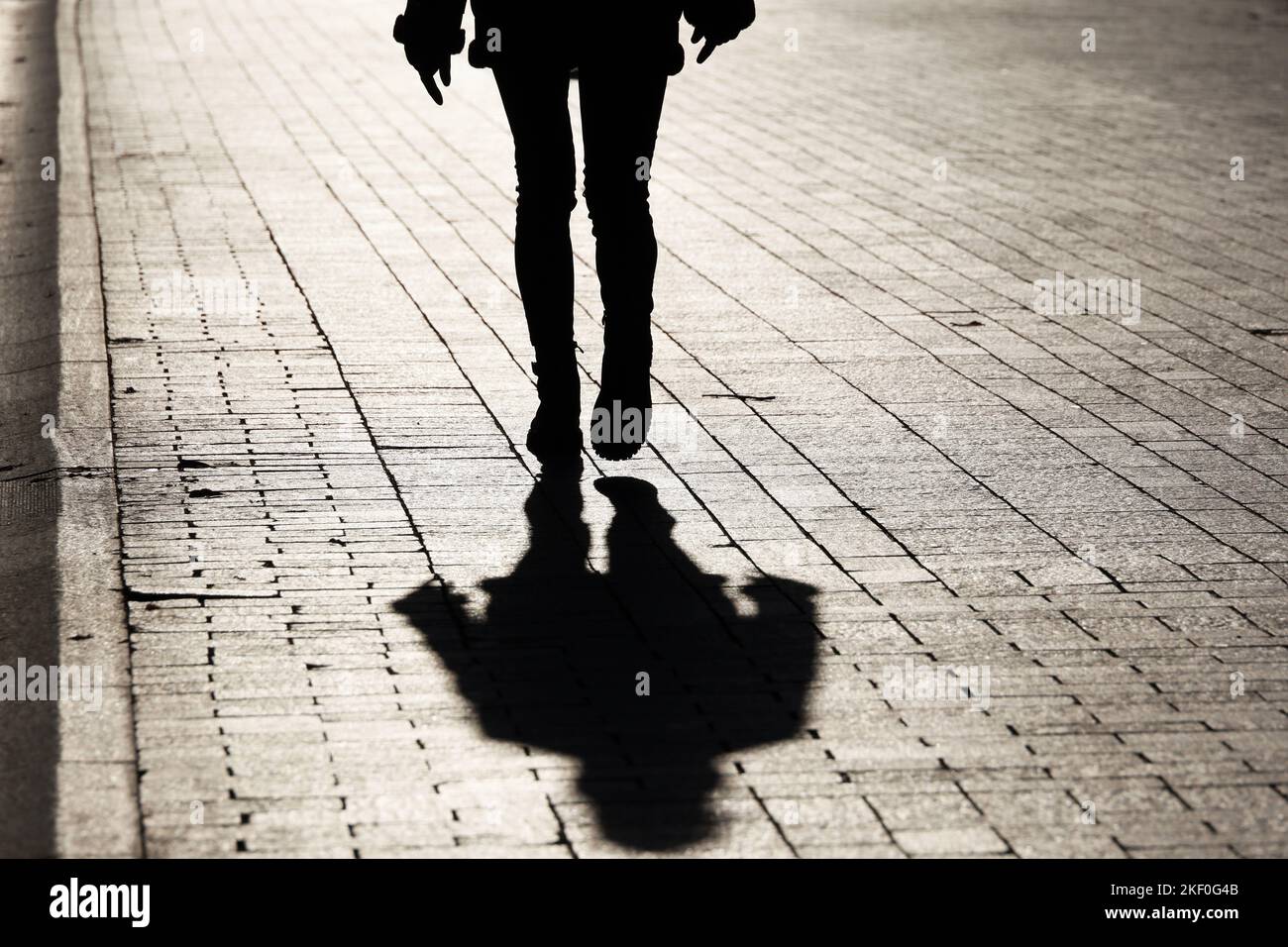 Black silhouette and shadow of lonely slim girl walking on a street. Female legs in tight jeans and boots, dramatic life Stock Photo