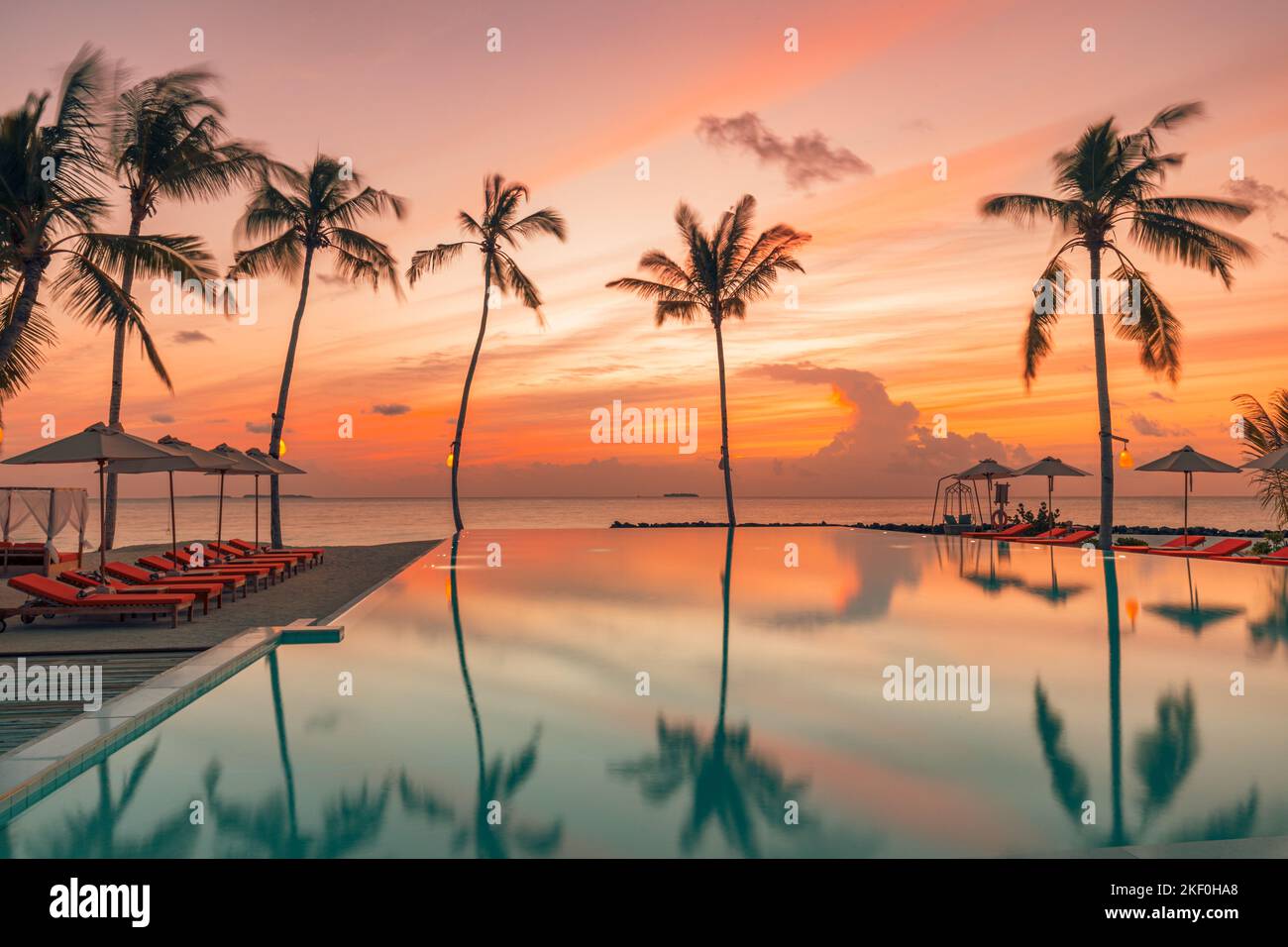 Fantastic poolside, sunset sky, palm trees reflection. Luxury tropical beach landscape, infinity swimming pool, deck chairs bed under umbrellas Stock Photo