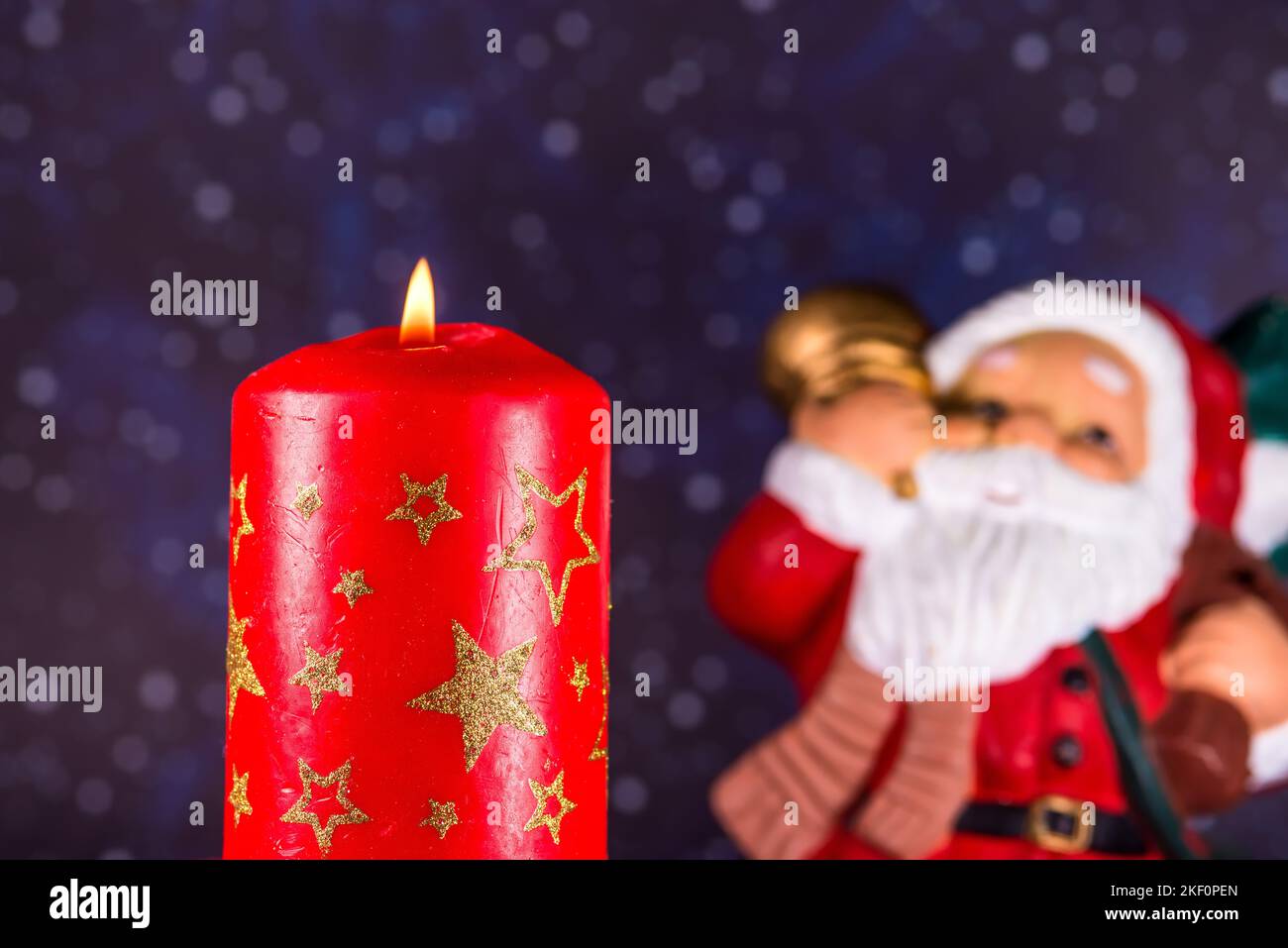burning candle with Santa Claus in the background Stock Photo